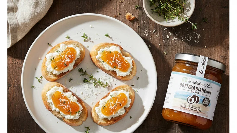 Quattro tartine con formaggio fresco e confettura di albicocca Bottega Bianchin su piatto bianco, timo e vasetto accanto